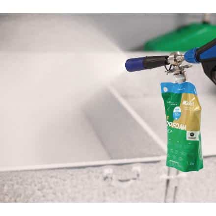 A hose nozzle spraying foam cleaner from an attached biodegradable pouch inside a large sink or industrial basin.
